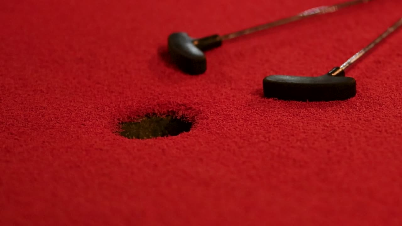 Una pallina da golf rossa rotola su un percorso in miniatura ruvido, mancando di poco la buca