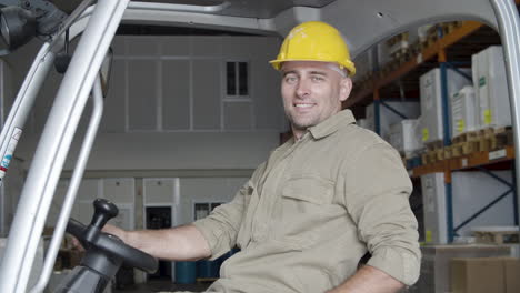 happy caucasian male worker sitting in forkfit and looking at the camera