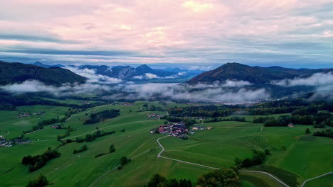 Luftaufnahme-Einer-Grünen-Landschaft-Mit-Wenigen-Clustersiedlungen-Im-Tal-In-Der-Nähe-Hoher-Berggipfel-Unter-Bewölktem-Himmel