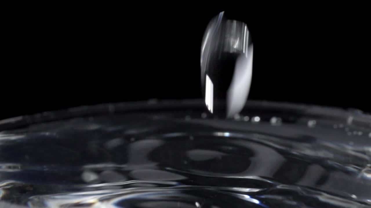 Macro shot of water drops continuously falling into a full glass