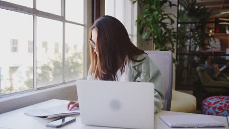 millennial asian female creative sitting at a desk working on a laptop in a casual office, close up