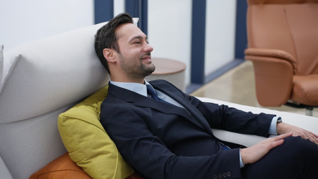 Successful Businessman checking mobile phone relaxing on a couch in a positive mood with a satisfactory smile and confidence