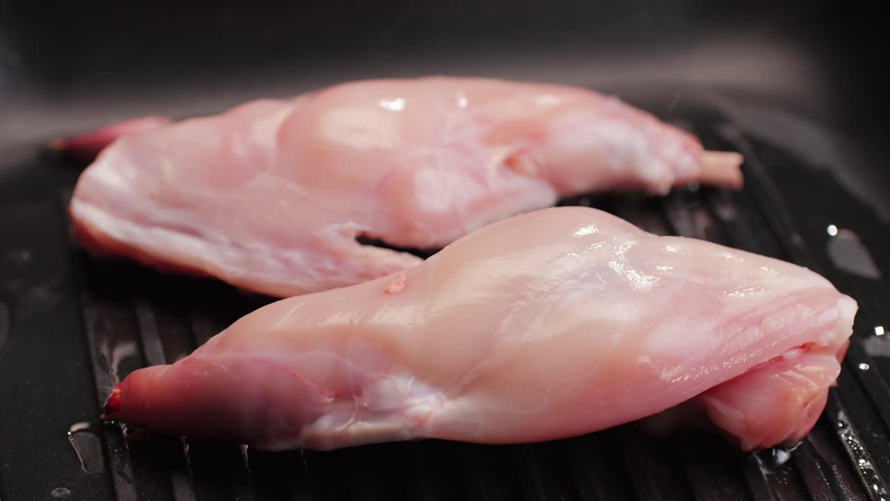 Cosce di coniglio arrosto in una padella grill, primo piano di carne salutare per la dieta, chef che cucina coniglio nella cucina del ristorante, sfondo nero. Vista dall'alto