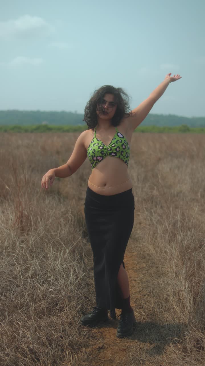 Woman adjusting top in dry grass field on sunny day, relaxed and casual vibe