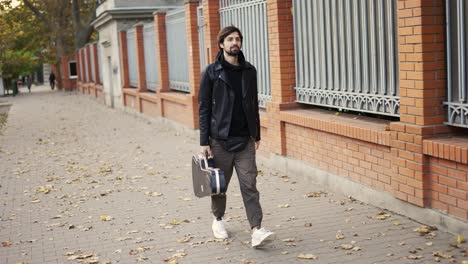 man walk down the street holding a guitar case