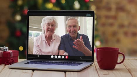 Caucasian-senior-couple-waving-on-video-call-on-laptop,-with-christmas-tree