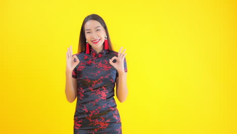 a young woman dressed in a black and red silk print dress flashes a big smile and the ok sign