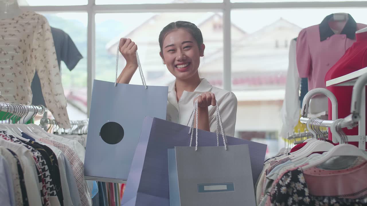 부티크에서 쇼핑하는 동안 카메라에 미소 짓는 쇼핑 가방을 가진 젊은 아시아 여성