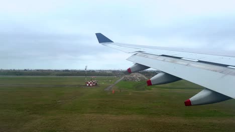 Airplane-wing-over-green-fields-during-landing-approach,-cloudy-skies