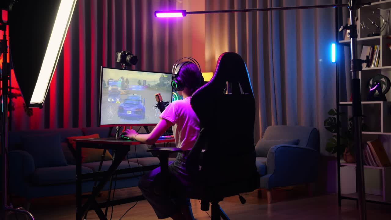 vista trasera de una chica asiática que se estira mientras juega a un juego de carreras de coches a través de la red en una computadora personal. videojuego de transmisión en vivo, escritorio iluminado por luz de tira led rgb