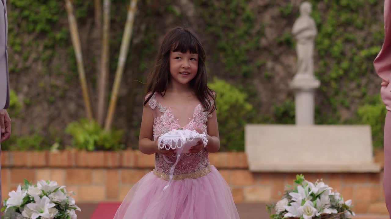 A young girl presents wedding rings on a pillow during a ceremony