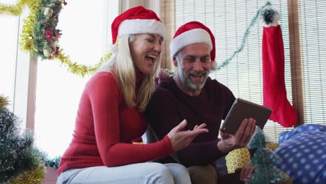 Happy-caucasian-mature-couple-making-video-call-in-room-full-of-christmas-decorations