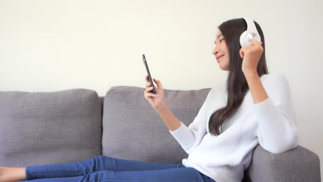 Bonita-Mujer-Asiática-Escuchando-Música-Con-Smartphone-Y-Auriculares-Inalámbricos-Con-Los-Dedos-Chasqueando-Al-Ritmo-De-La-Música,-Cámara-Lenta-De-Cuadro-Completo