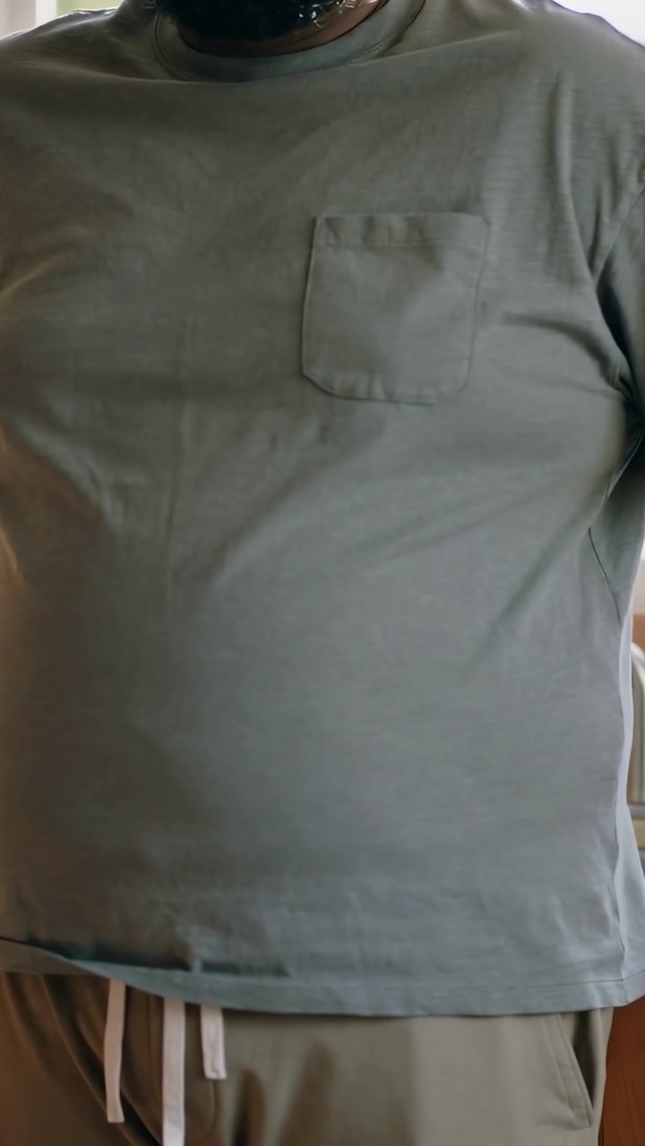Vertical video: Breathing man in pocket tee drawstring necklace shifting torso at kitchen window