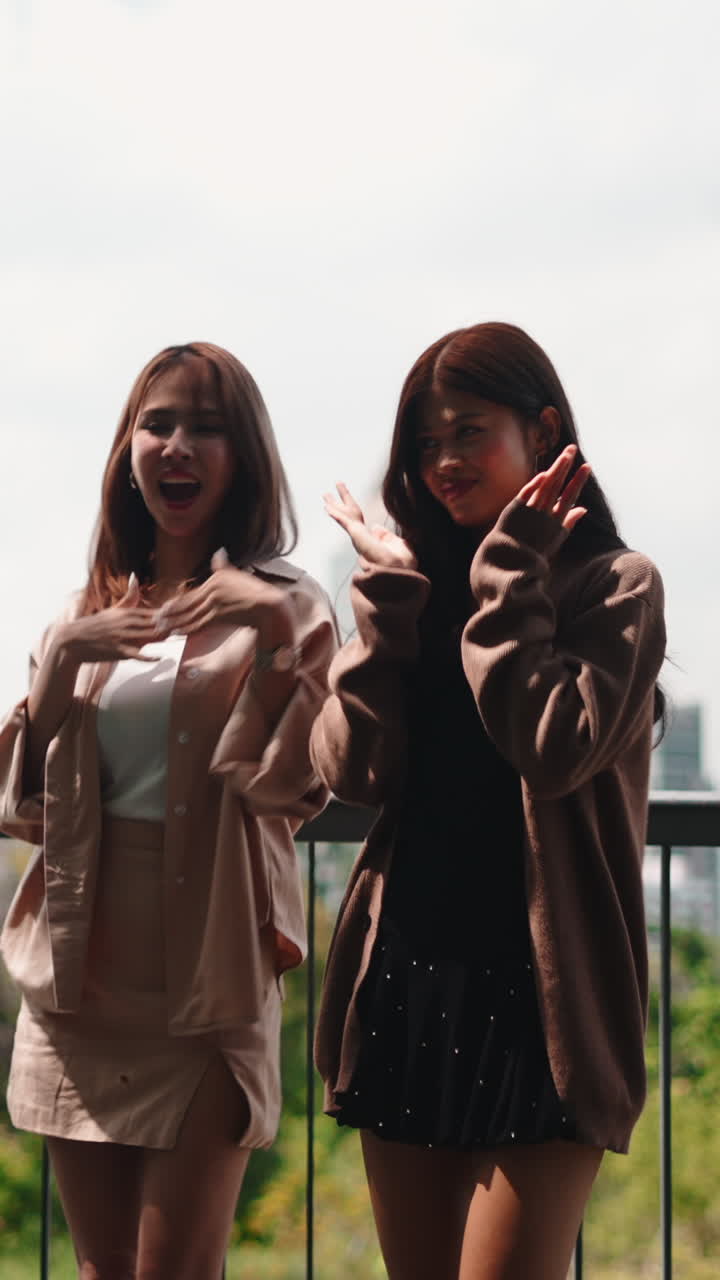 Dos mujeres jóvenes bailando y sonriendo en un balcón