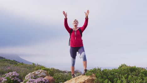 senior hiker woman standing with her arms wide open standing on a rock