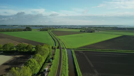 Following-a-train-track-in-a-Dutch-polder-landscape-with-a-drone-towards-the-Moerdijk-bridge