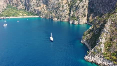 Luftdrohne-Nähert-Sich-Einem-Großen-Segelboot,-Das-In-Der-Bucht-Von-Butterfly-Valley-Angedockt-Ist,-Umgeben-Von-Türkisblauem-Ozean-Und-Großen-Bergen-In-Fethiye,-Türkei