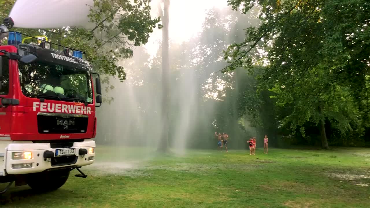camión de bomberos alemán rociando agua para niños y árboles en un caluroso día de verano-10