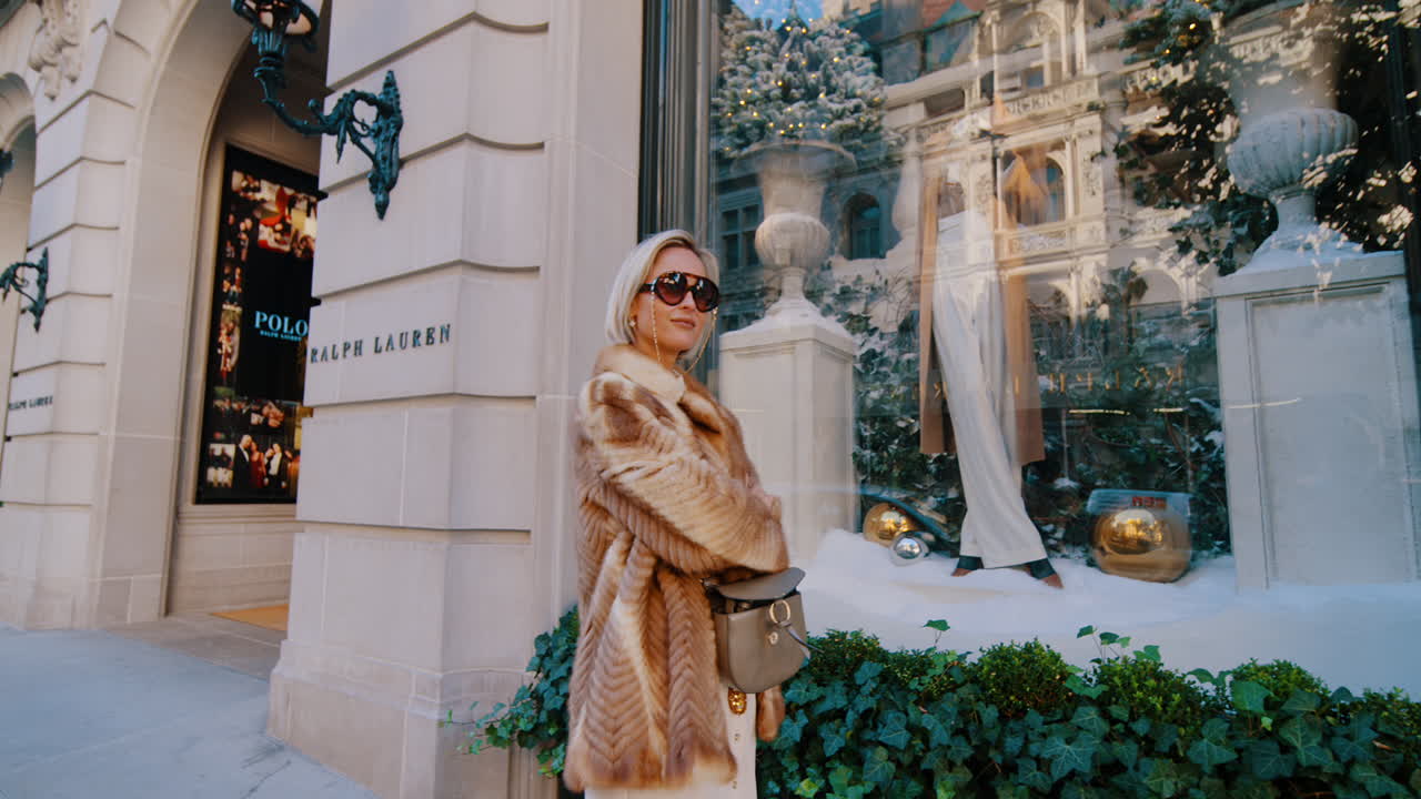 New York, USA, 5. oktober 2025: Kvinde i pelsfrakke står ved luksusbutiksvindue. Kvinde i stribet pelsfrakke og solbriller poserer nær eksklusiv butiksfacade på Fifth Avenue