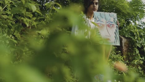 enfoque selectivo toma de cámara lenta cinematográfica de una joven asiática feliz sentada en la naturaleza, sosteniendo una pintura mientras mira frente a la cámara