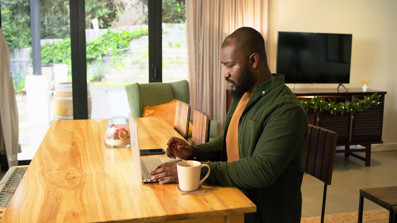 African American man typing on laptop at dining table feeling stiffness stretching arms, copy space