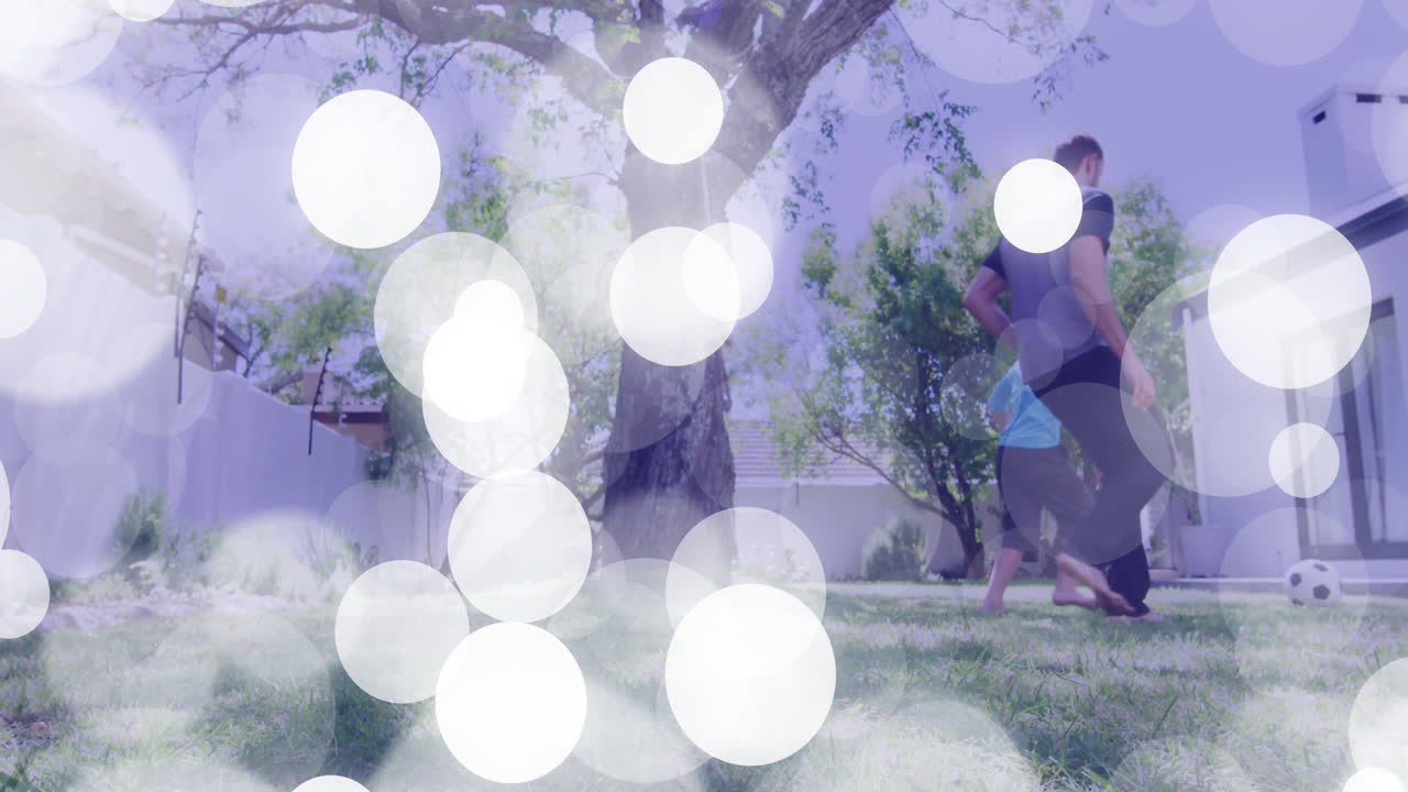 Father and son kicking soccer ball on grass lawn, showing animated health icon and fitness chart