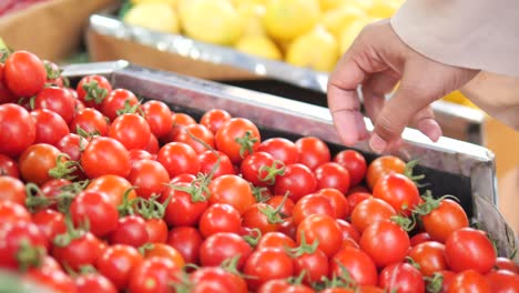 a hand picks up a cherry tomato from a display at a market.