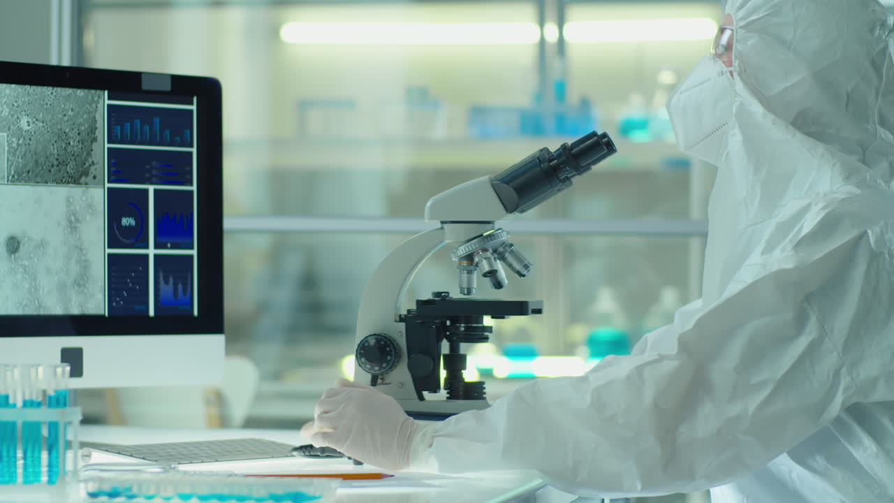 Scientist in Protective Suit Using Microscope in Lab
