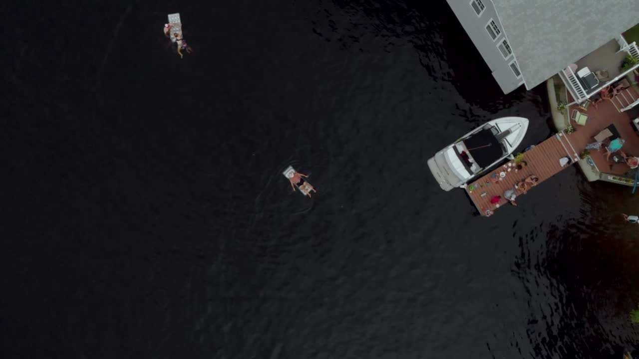 a man relaxing on a float while others hang out on a dock next to their cottage on summer vacation