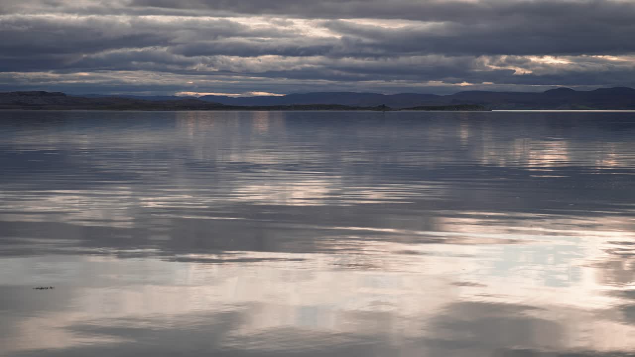 태양에 의해 백라이트 된 무거운 구름이 조용한 물 위에 매달려 있습니다.