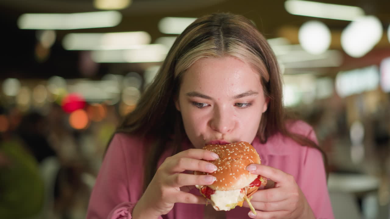 dama de vestido rosa toma un bocado de hamburguesa, masticando lentamente mientras contempla el sabor, se ve reflexiva mientras saborea la comida, el fondo presenta efectos de luz bokeh borrosos