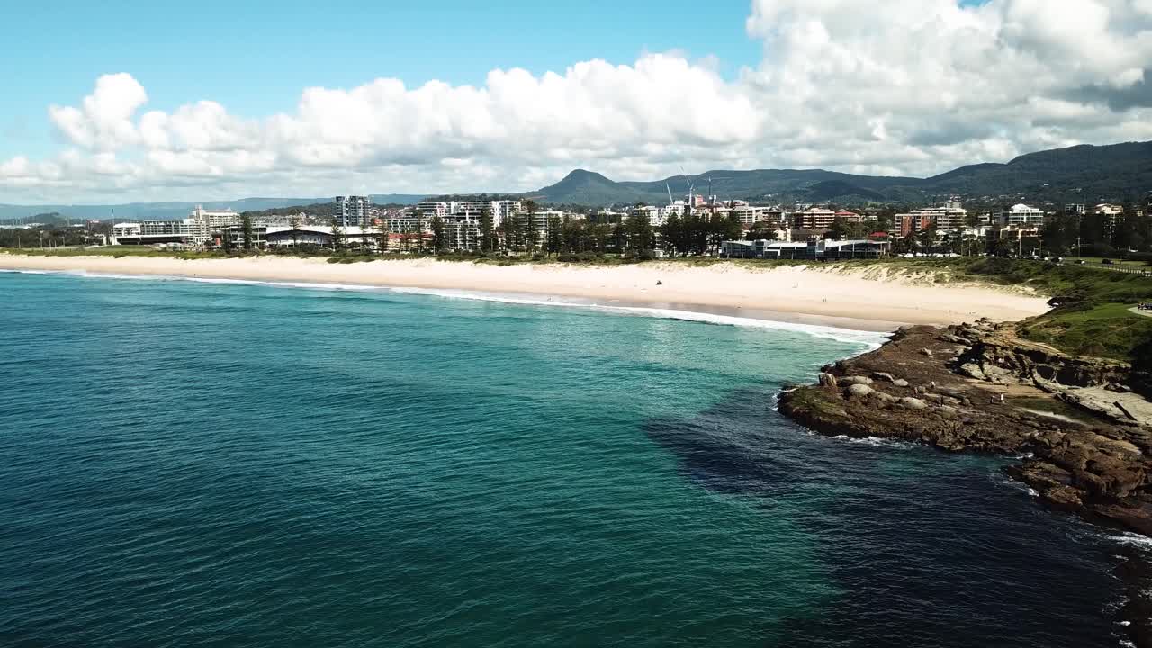 Drone is slowly flying above ocean and reveals beautiful city of Wollongong in Australia.