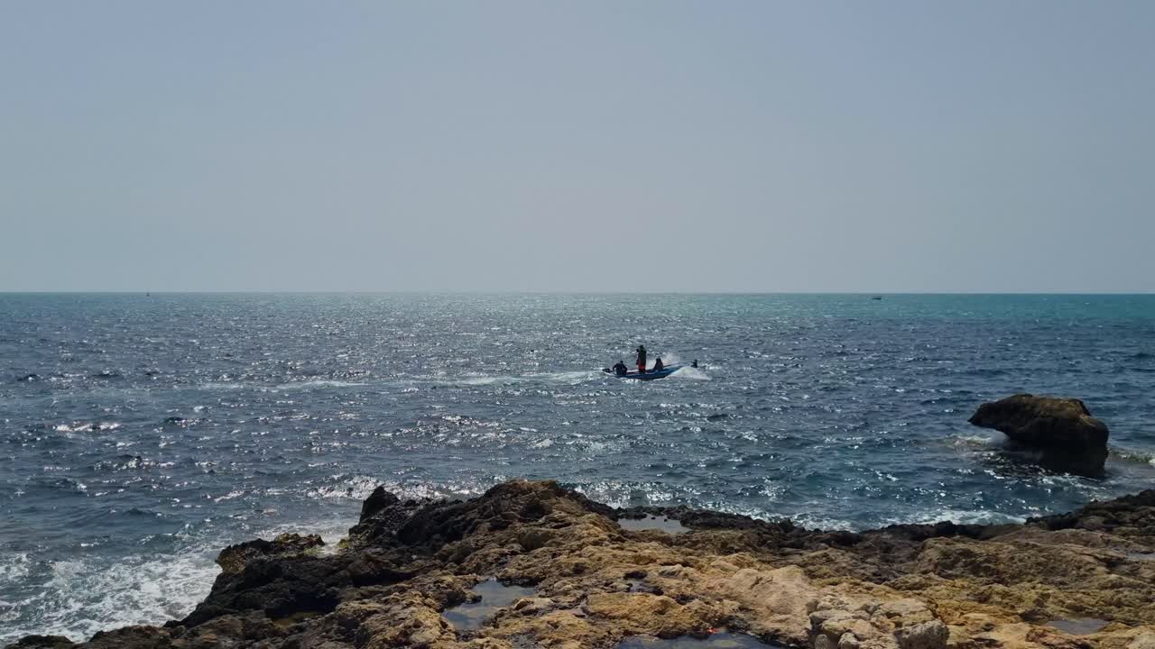 A small fishing boat glides past rocky shores near Hammamet, Tunisia, on a sunny day, with tranquil Mediterranean waters and a distant horizon in view