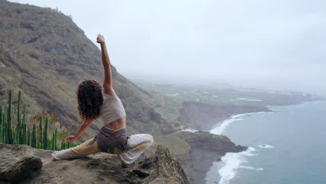 posicionada en un acantilado, una mujer asume una postura de guerrera, extendiendo sus brazos e inhalando el aroma del océano, encontrando tranquilidad a través del yoga