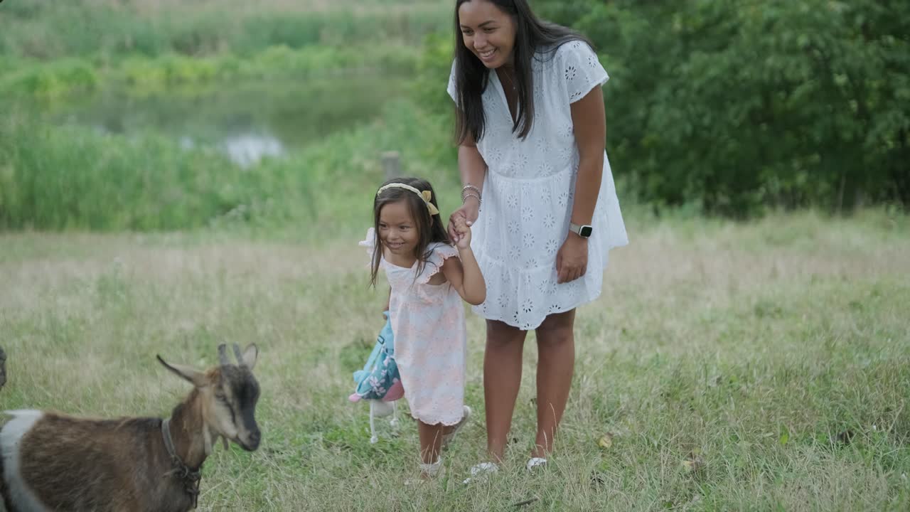 беременная женщина и ее маленькая дочь, одетые в белое, ходят рука об руку по травяному парку. сцена захватывает спокойный момент семейной связи в природе, окруженной деревьями.