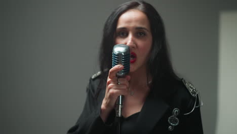 close-up of a female vocalist in a black outfit, holding a vintage mic with one hand, singing with a serious expression as the camera zooms in and out against a blurry background