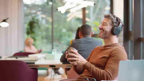 Businessman-With-Feet-On-Desk-In-Office-Listens-To-Music-On-Wireless-Headphones--Catching-Football