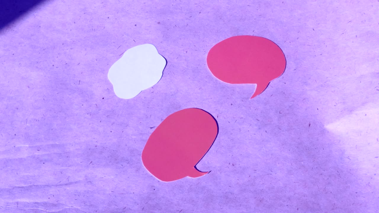 4k video, close-up of two pink speech bubbles cut out of paper and a white cloud with space for text. Turn on lilac kraft paper, top view