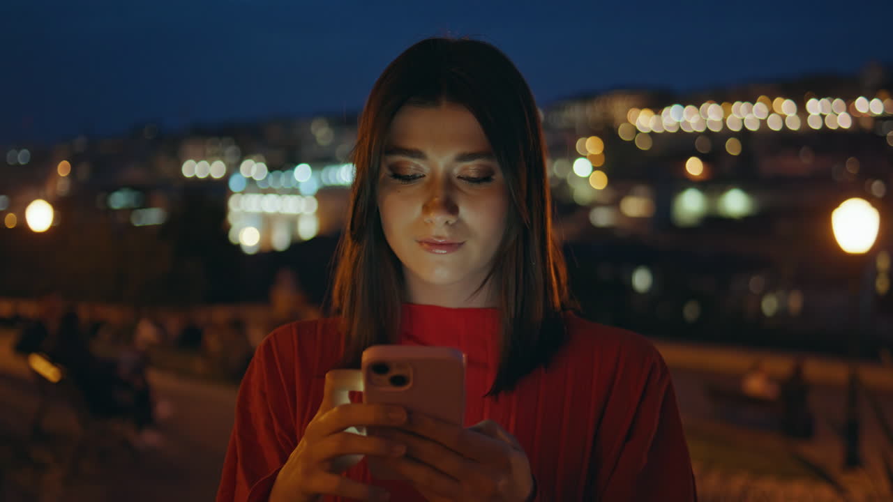 Primo piano di una donna sorridente che digita sul cellulare in una strada cittadina di sera. Donna che risponde a un SMS.