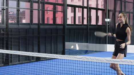 woman playing padel tennis on indoor court, holding racket and smiling