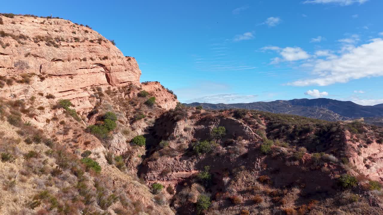 Aerial drone footage of rugged sandstone cliffs and desert vegetation, showcasing dramatic shadows and terrain contours beneath a vibrant blue sky