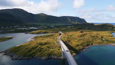 following the black car driving along the fredvang bridge in lofoten northern norway with the light turquoise blue sea ocean water towards the mountains on the horizon and green yellow grass below