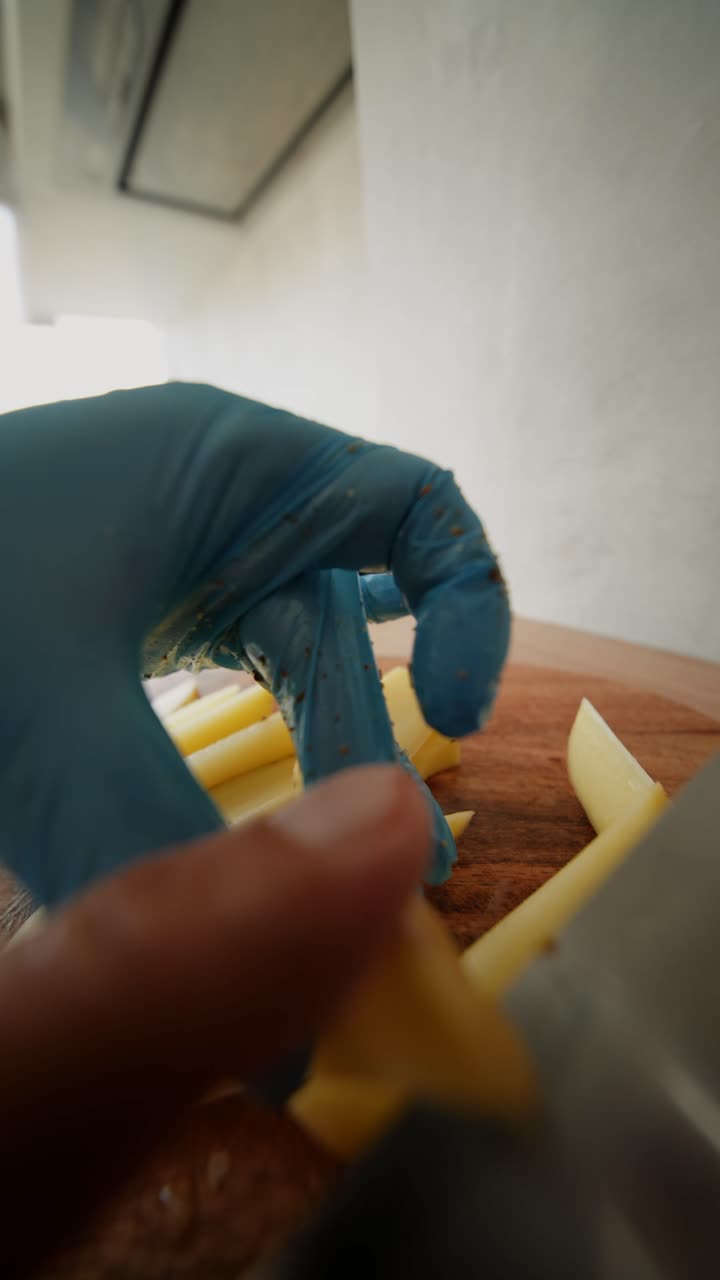 Close-up of Hands in Gloves Slicing Potatoes on a Cutting Board