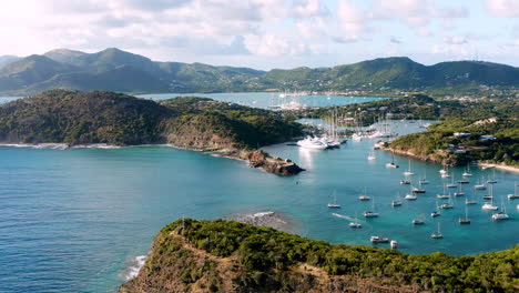 toma aérea soleada del puerto inglés en antigua, caribe con vistas de yates, veleros, puerto deportivo, bahía y acantilados