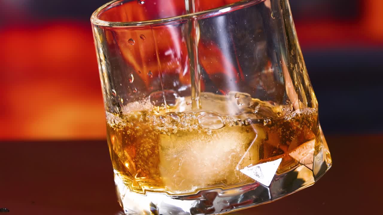 Close-up of a golden beverage swirling around ice cubes in a faceted glass.