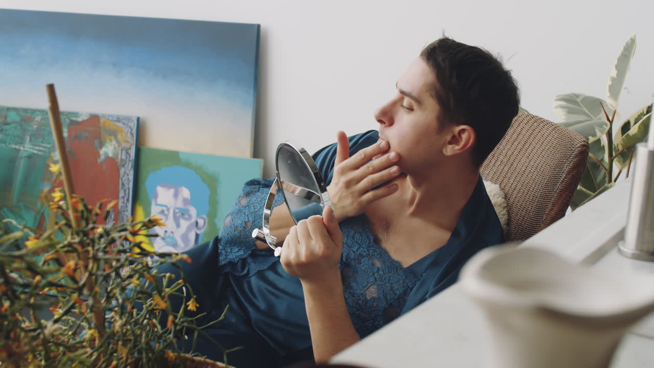 hombre transgénero sentado en casa y aplicando crema en la cara