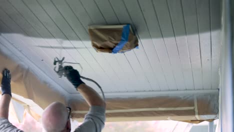 house painter applying white paint to house ceiling with an airless paint sprayer