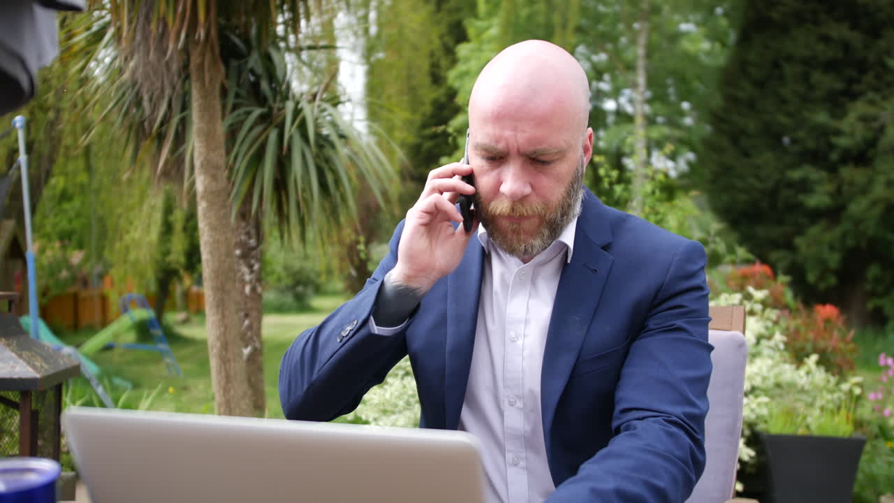 En forretningsmand besvarer telefonen, mens han bruger sin bærbare computer i sin have derhjemme