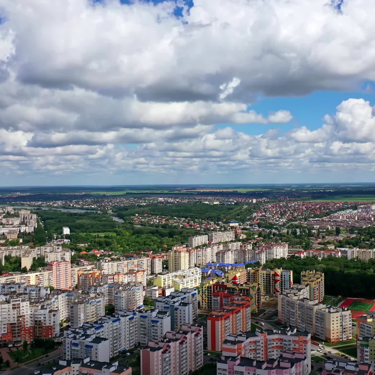 Urban background under beautiful sky. Modern city with high-rise buildings on green fields background. Aerial view. Camera rising up.